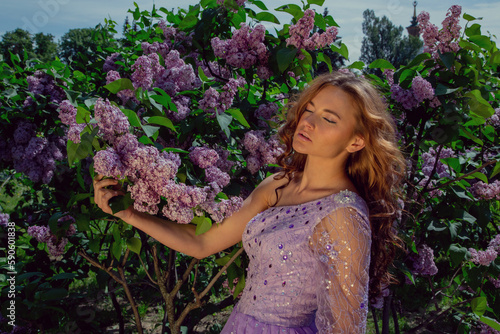 Spring style. A young woman in a beautiful dress in a garden with blooming purple bushes. Blooming spring garden.