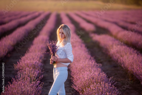 Wallpaper Mural Young woman in white shirt, blue jeans stays in rows of purple lavender in field. Millennial girl holding bouquet of flowers in hands at sunset. Allergy concept. Production natural perfumery. Torontodigital.ca