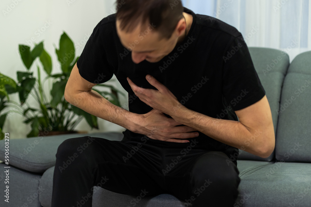Man suffering with severe stomach pain sitting at home. Hand of mature guy holding abdomen suffering from ache, diarrhea or indigestive problem. Caucasian guy pressing on belly on painful sensation Man suffering with severe stomach pain sitting at home. Hand of mature guy holding abdomen suffering from ache, diarrhea or indigestive problem. Caucasian guy pressing on belly on painful sensation