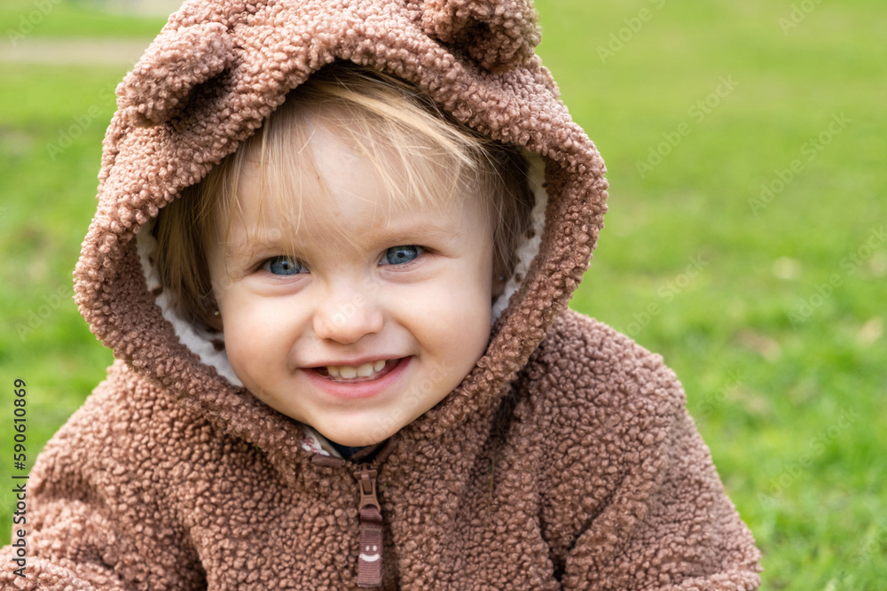Portrait of a one-and-a-half-year-old blue-eyed girl in a bear costume in a park on the grass Portrait of a one-and-a-half-year-old blue-eyed girl in a bear costume in a park on the grass
