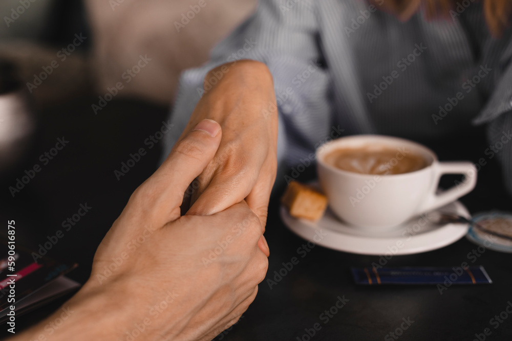 Female palm in the hand of man, at a table with coffee. Psychological support, romantic date concept. Couple having a coffee time while holding hands. Couple drinking coffee at cafe restaurant.