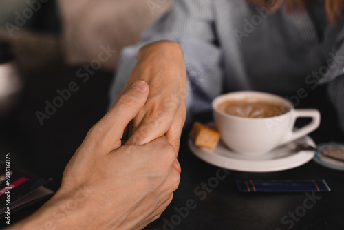 Female palm in the hand of man  at a table with coffee. Psychological support  romantic date concept. Couple having a coffee time while holding hands. Couple drinking coffee at cafe restaurant.