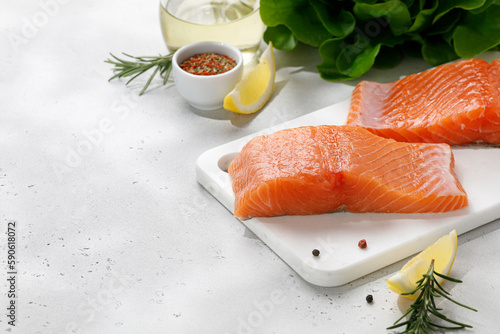 Salmon. Fish steaks, slices. Raw uncooked salmon fillet fish with rosemary, lemon and pepper on white cutting board and grey background.