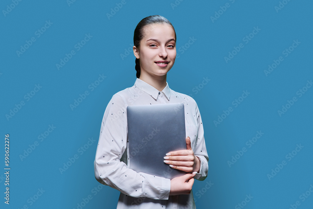 Teenage girl holding closed laptop in her hands, on blue studio background Teenage girl holding closed laptop in her hands, on blue studio background
