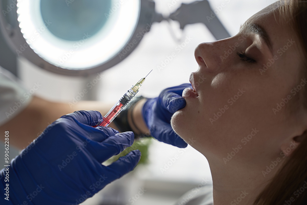 Lip augmentation and correction procedure in a cosmetology salon. The specialist makes an injection in the patient's lips