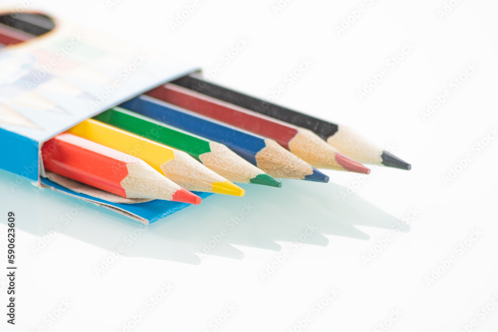 Office theme. Colored pencils in an open box lie on a white mirror background