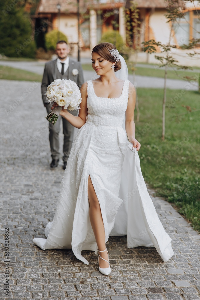 Stylish young brides, happy on their day, enjoy each other. They are walking in the spring park. The groom is behind the bride. Spring wedding. Natural makeup