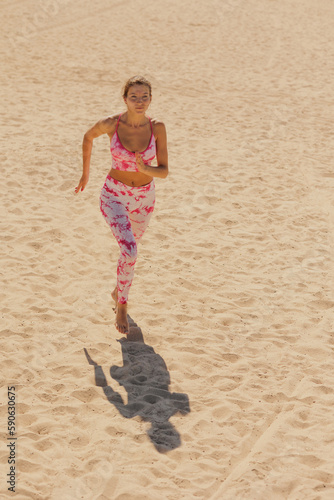 athletic woman in sportswear runs along sandy beach. sporty lady prepares for marathon do fitness, stretching and yoga outdoors. healthy lifestyle, strong muscles and back. confident female champion
