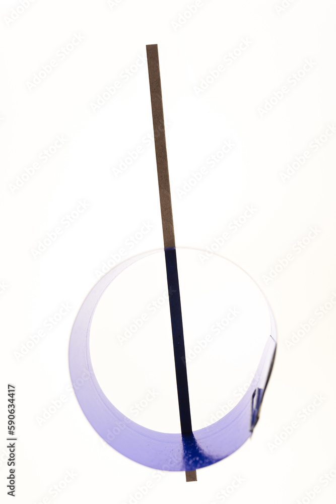 isolated on a white background are two objects a thin brown cardboard stripe and a circular or ring in metallic blue isolated on a white background are two objects a thin brown cardboard stripe and a circular or ring in metallic blue