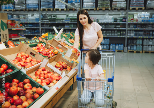 Family in the supermarket. young mother and her little daughter are smiling and buying food. Healthy food concept. mom and daughter buy vegetables and fruits in the supermarket