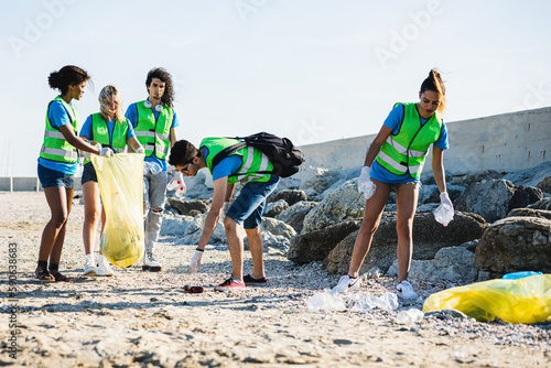 Diverse people cleaning up the beach, volunteers collecting the waste on the coast line, young people working in team aware of of human made pollution