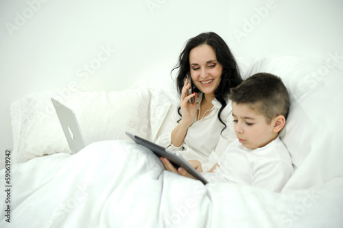 cute baby looking the mobile phone with mother and sitting on the bed. High quality photo