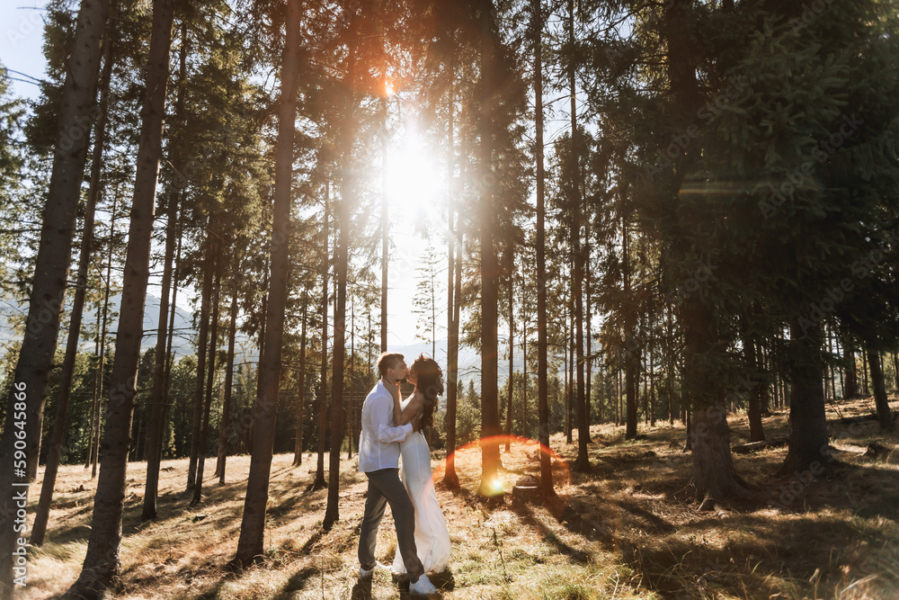 Obraz premium Stylish model couple in white clothes kissing at sunset in the forest. A girl hugs her husband, hair blowing in the wind. Wide angle photo