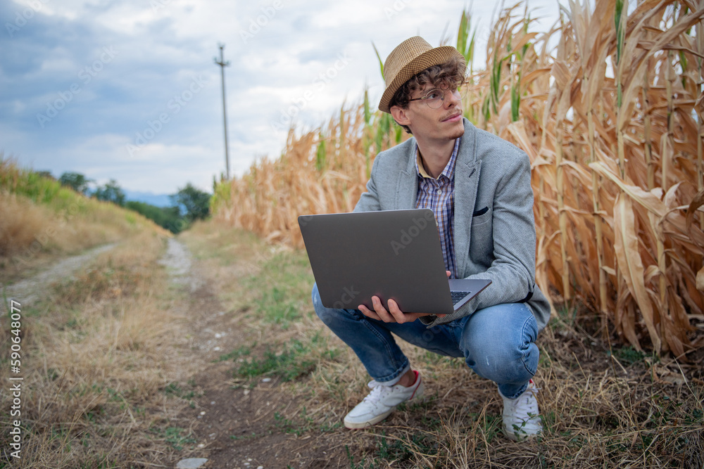 A young stylish creative artist holds up his laptop and kneels as he looks around A young stylish creative artist holds up his laptop and kneels as he looks around