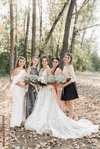 Wedding photo in nature. The bride and her bridesmaids are standing in the forest smiling, holding theirs bouquets and looking into the camera lens. Happy wedding concept. Emotions. girls © Vasil