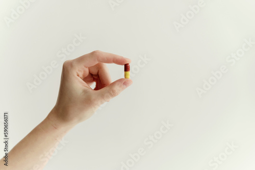 close-up of a hand holding a pill in the fingers on an isolated white background. one tablet red-yellow shell. medicine