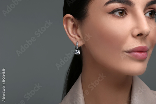 Beautiful young woman with elegant earrings on dark grey background, closeup