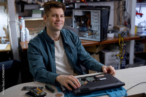 professional young repairman or technician repairs computers and laptop. portrait of service engineer in shirt repairing a laptop, happy guy looking at camera, posing, successful job