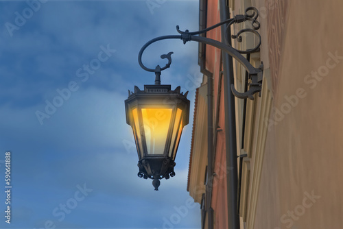 Turned on hanging street lamp in old fashion style on building