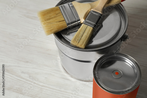 Can of orange paint, bucket and brushes on white wooden table, closeup. Space for text