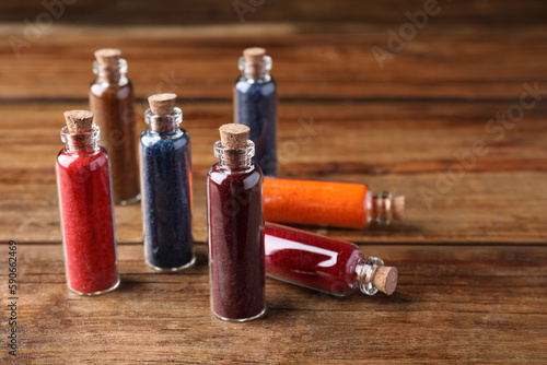 Glass bottles with different food coloring on wooden table. Space for text