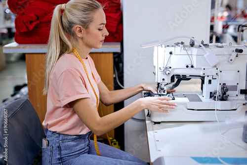 focused blonde caucasian female seamstress sits using modern sewing machine. Dressmaker works in textile workshop. Tailoring, sewing as a small business or hobby concept. sewing process photo