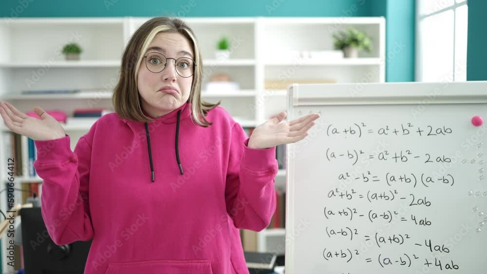 Young blonde woman student standing with arms crossed gesture and i dont know expression at library university