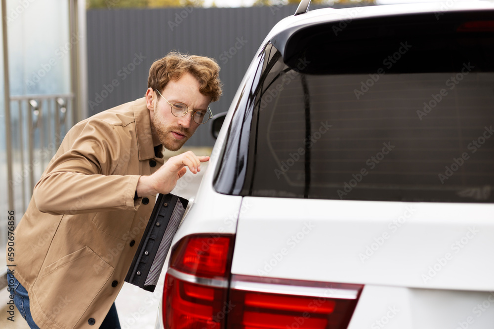 Handsome man carefully wiping car with window scraper. Concept of self-service wash car