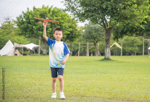 A little boy playing with a plane on the park lawn