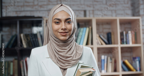 Photography Female muslim student in library, holding books and looking at camera, girl wear