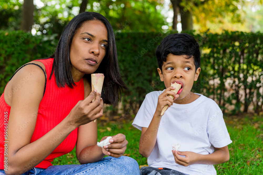 Mother and son enjoying eating ice-cream together outdoors in a park. Mother and son enjoying eating ice-cream together outdoors in a park.