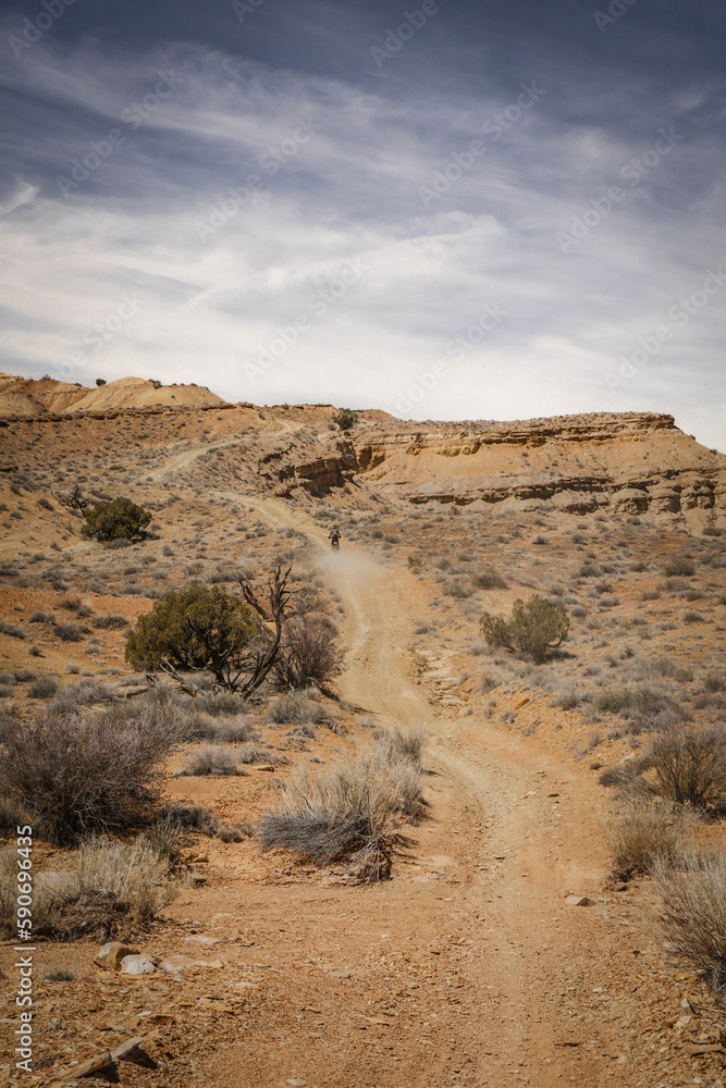 Wide dirt road through desert terrain in spring in central Utah near Goblin Valley underneath  rocky cliffs and mesas
