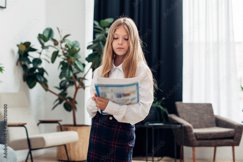 Elementary school girl stands with a textbook and looks at the camera Elementary school girl stands with a textbook and looks at the camera