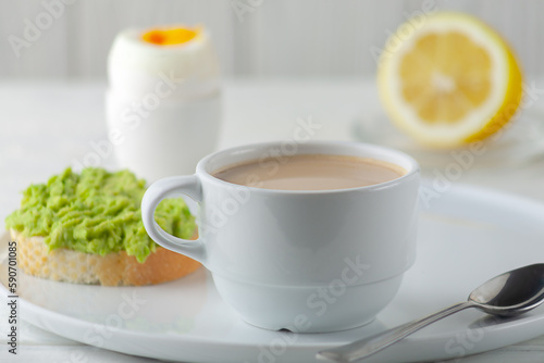 A cup of coffee with cream and a soft-boiled egg with an avocado sandwich on the table. European breakfast.