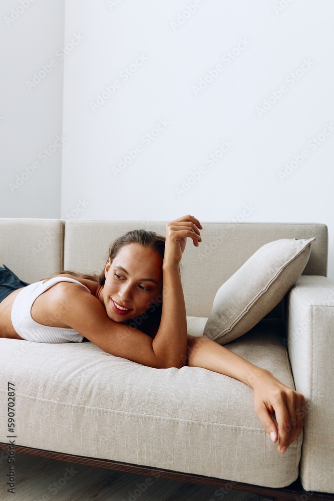 A woman lies relaxed on the couch and smiles looking at the camera in home clothes with long hair and tanned skin A woman lies relaxed on the couch and smiles looking at the camera in home clothes with long hair and tanned skin