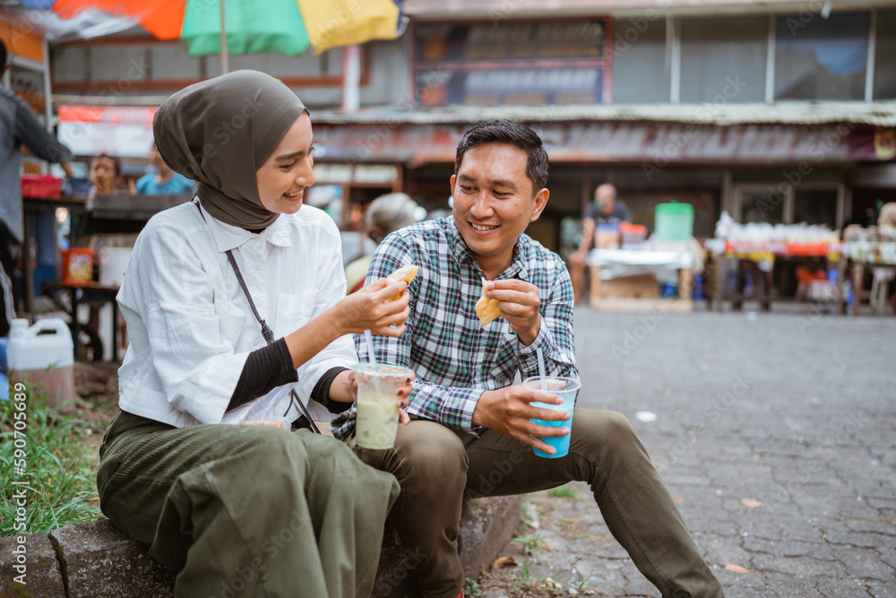 beautiful muslim couple sitting on a road side and enjoy the food they bought from street vendor during ramadan