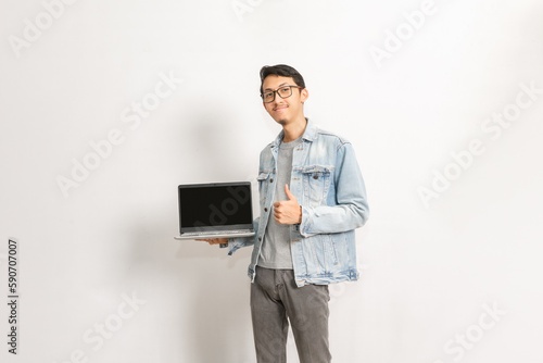A man shows his laptop display and gives his thumb up. Indonesian or southeast asian model isolated with white wall background.