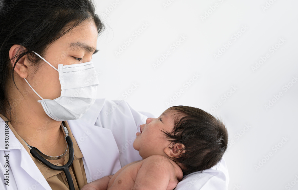 Asian doctor holding cute newborn baby in her arms for physical check up in clinic.