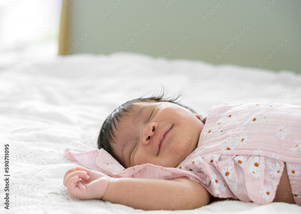 Smiling new born adorable baby girl sleeping on white bed at home Smiling new born adorable baby girl sleeping on white bed at home
