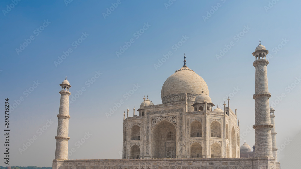 Majestic white marble Taj Mahal against the blue sky. A beautiful symmetrical mausoleum with arches, domes, spires, minarets. India. Agra