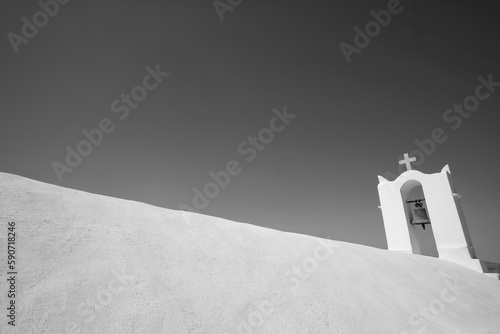 A cross on the top of an orthodox whitewashed church in Ios Greece and a blue sky in the background in Ios Greece in black and white