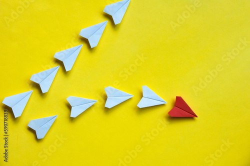 Red paper airplane origami leaving with other white airplanes on yellow background with customizable space for text or ideas. Leadership skills concept and copy space