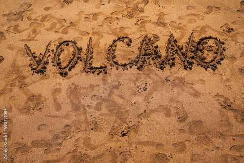 Text VOLCANO on volcanic sand. Texture, wave pattern of ocean sand on the beach. Texture of beach sand. Volcanic beach
