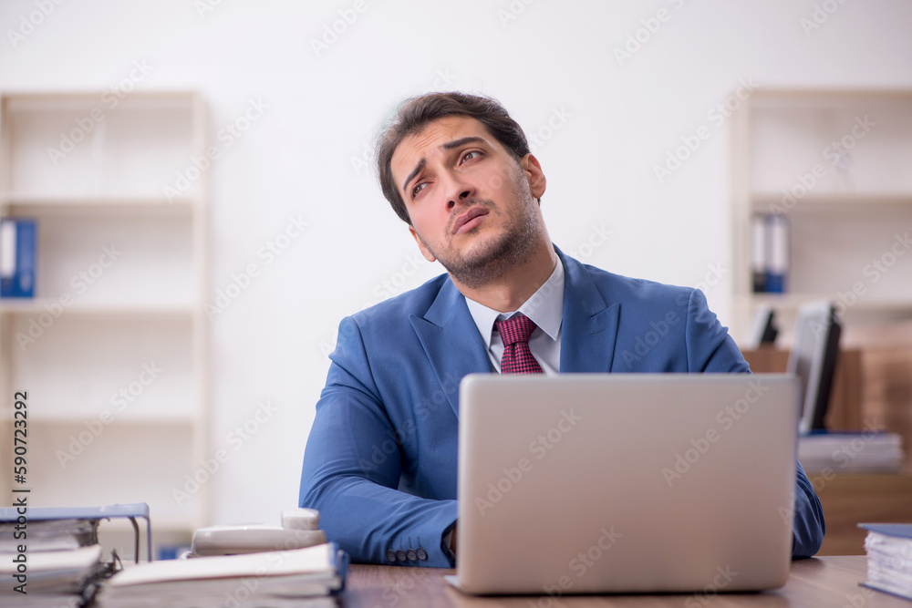 Young male employee unhappy with excessive work in the office Young male employee unhappy with excessive work in the office