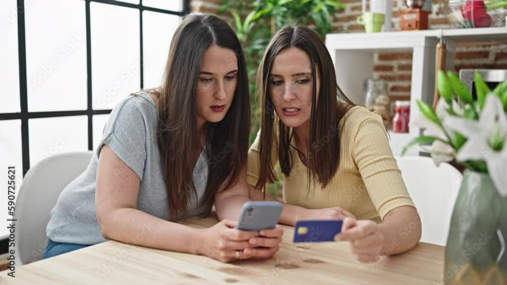 Two women shopping online with smartphone and credit card at dinning room Two women shopping online with smartphone and credit card at dinning room