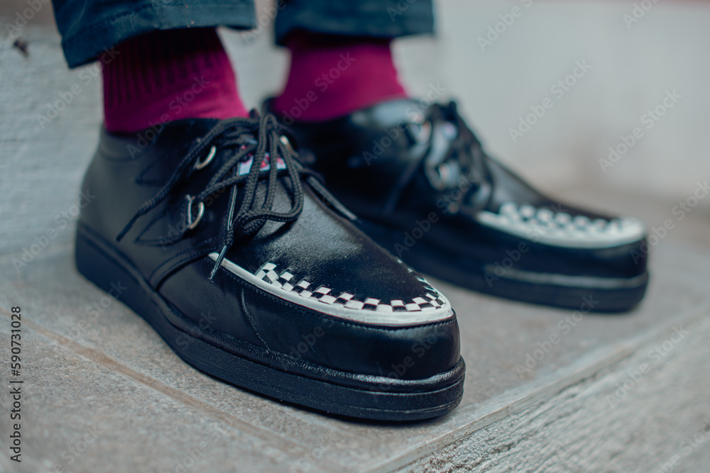 Young man sitting and wearing black genuine leather creepers sneakers. These casual yet elegant shoes are handmade by an at-home shoemaker, perfect for hanging out on a sunny day Young man sitting and wearing black genuine leather creepers sneakers. These casual yet elegant shoes are handmade by an at-home shoemaker, perfect for hanging out on a sunny day