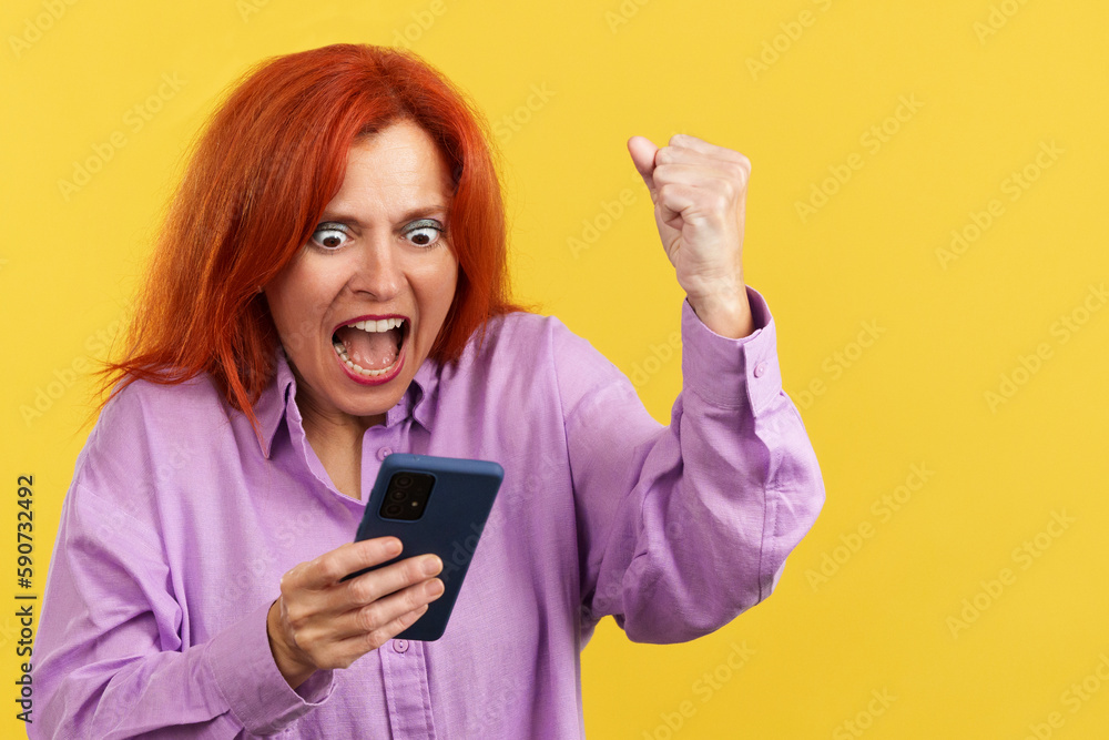 Excited mature redheaded woman celebrating while using the mobile phone Excited mature redheaded woman celebrating while using the mobile phone