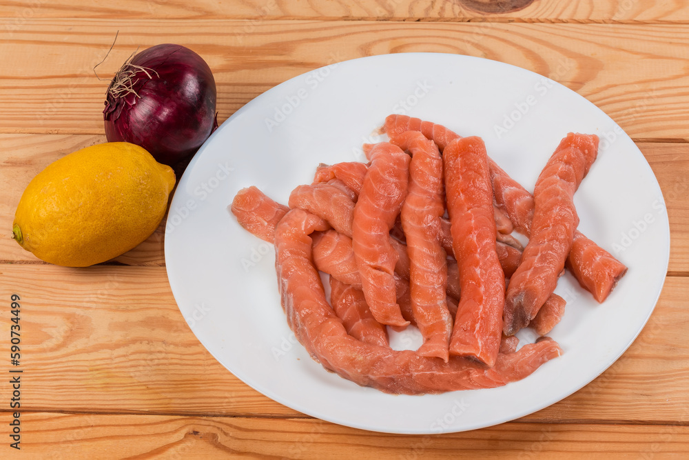 Long raw salmon slices, onion and lemon on rustic table
