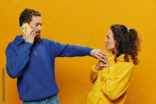 Woman man cheerful couple with phones in hand social networking and communication crooked smile fun and fight, in yellow background. The concept of real family relationships, freelancers, work online.