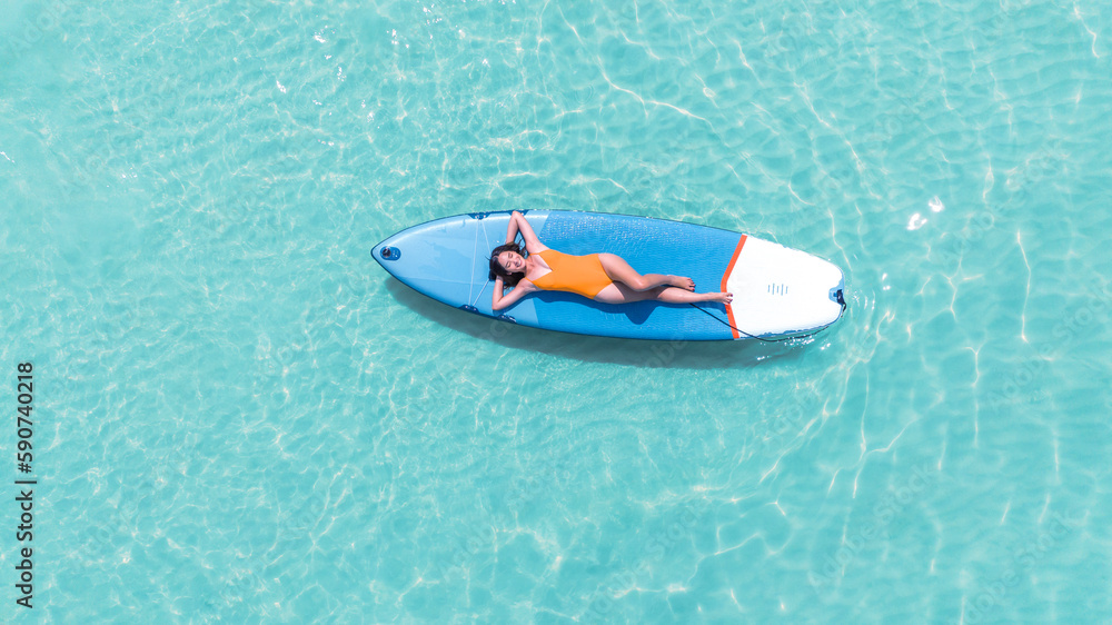 Asian woman in bikini sleep and relax on paddle board on the beach